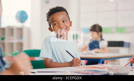 Portrait Of Smiling Male Elementary School Student Sitting At Table Painting Stock Photo