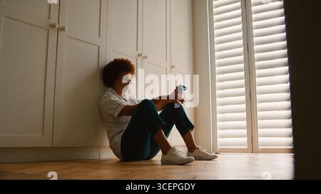 Unhappy And Demotivated Nurse Wearing Uniform Sitting On Floor At Home After Long Shift Stock Photo
