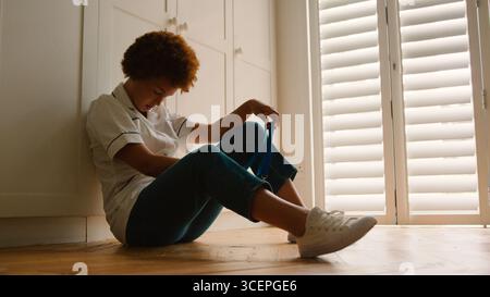 Unhappy And Demotivated Nurse Wearing Uniform Sitting On Floor At Home After Long Shift Stock Photo