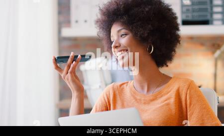 Young Smiling Businesswoman Working At Desk In Office Talking Into Mic Of Mobile Phone Stock Photo