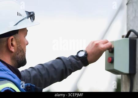 A worker in a white helmet presses the start button on a box with buttons. Stock Photo