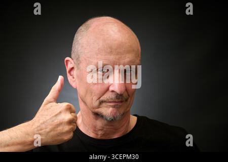 Closeup portrait of a elderly man in studio with thumbs up in a vintage Harcourt style lighting Stock Photo