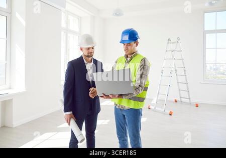 Construction engineer, architect colleague looking at project online on laptop, blueprints, planning Stock Photo
