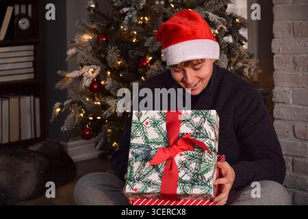 Young man in Santa hat looks happy and surprised when opening Christmas present Stock Photo