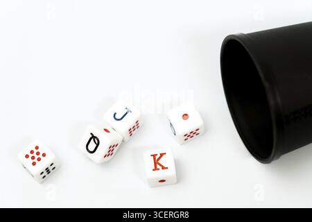 Poker dice spilling from a black dice cup onto a white background, representing gambling and games of chance Stock Photo