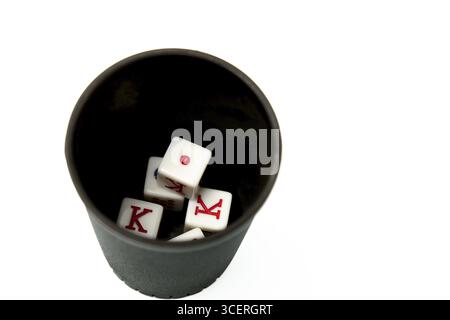 Four white dice showing king and one resting in a black dice cup on a white background, suggesting gambling and games of chance Stock Photo