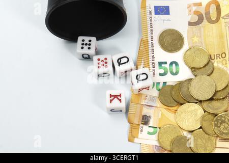 Poker dice spilling from a black cup onto a pile of fifty euro banknotes and coins, symbolizing gambling, risk, and investment Stock Photo