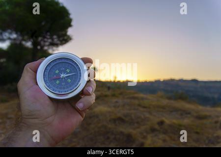 Hand is holding a compass showing direction at sunset in the nature Stock Photo