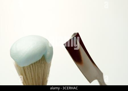 Shaving brush with light blue foam and straight razor on white background, getting ready for skincare routine Stock Photo