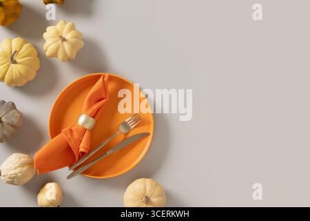 Autumn and Thanksgiving Day table setting with white small pumpkin, orange empty plate with golden cutlery on gray background. Concept catering. Top v Stock Photo