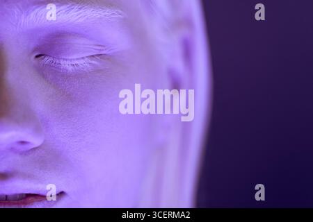 Macro close-up studio shot of young Caucasian woman with albinism standing with eyes closed in ultraviolet neon light Stock Photo