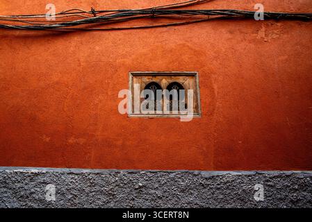 A rustic orange wall featuring an intricately designed wooden window and exposed electrical wires, showcasing a blend of textures and colors in urban Stock Photo