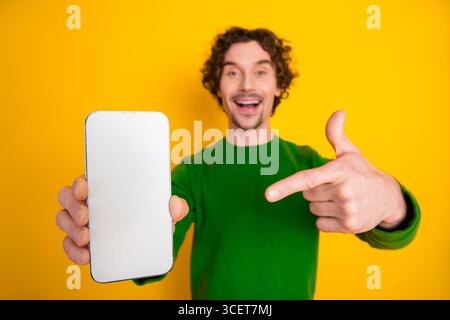 Happy man in vibrant outfit displaying smartphone with blank screen, showcasing advertising or app on yellow backdrop Stock Photo