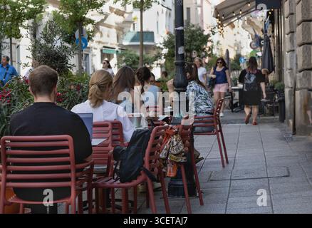 Guests sitting on the terrace of a café in downtown Budapest are enjoying their drinks. A man sitting with his back to the table is working on his lap Stock Photo