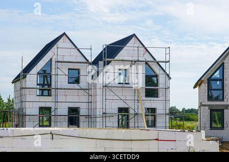 A modern two-story house in progress, featuring scaffolding, insulation panels, and unfinished exterior walls under a clear blue sky Stock Photo