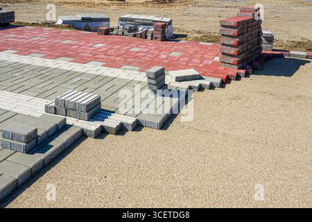 Paving stones arranged with tactile guiding blocks for visually impaired pedestrians. Red, gray, and white paving on sand foundation Stock Photo