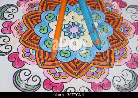 Blue and orange colored pencil lying on a colored mandala drawing Stock Photo