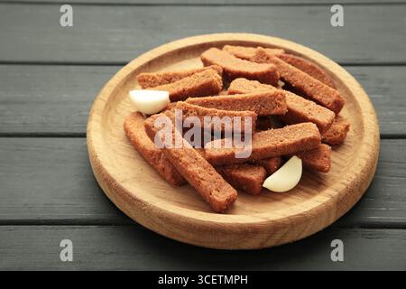 Tasty rye croutons on wooden plate on black background. Top view Stock Photo