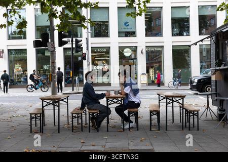 Two men in conversation whilst taking a coffee as they sit on benches along Waterloo Road, central London, England, United Kingdom Stock Photo