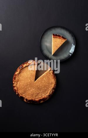 Whole cheesecake pie with one slice on black background and piece served on plate. Top view, flat lay. Stock Photo