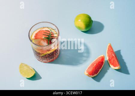 Glass of grapefruit cocktail with lime slices and rosemary on blue background with sharp shadows. Top view. Stock Photo