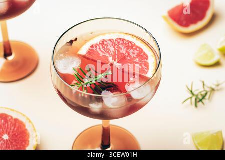 Close up of grapefruit cocktail with ice cubes and rosemary in glass on beige background. Closeup. Stock Photo