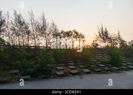 Mesmerizing sunlight streaming behind trees reflecting over abandoned coastal walkway in Patenga, Bangladesh Stock Photo