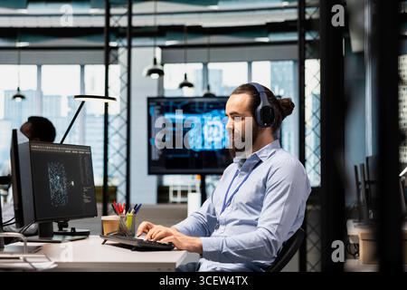 Programmer optimizing performance using AI LLM chatbot recommendations, listening music. Worker wearing headphones uses artificial intelligence assistant to automatize workflows Stock Photo