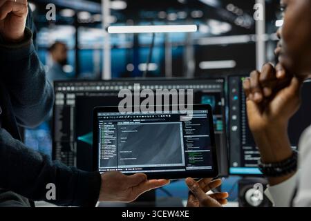 Close up of programmers coding on tablet in data center, refining algorithms for faster processing. IT workers using device in server room, conducting tests using software Stock Photo