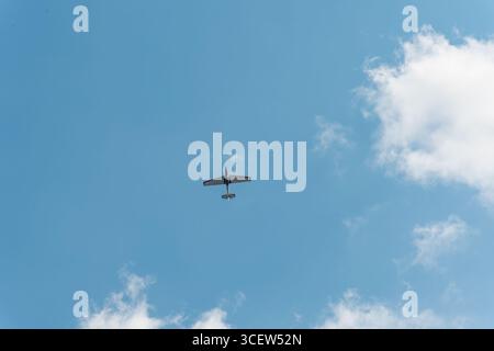 Airplane captured from below flying overhead in a blue sky with scattered white clouds, leaving large negative space Stock Photo