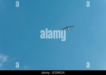 Minimal view of an airplane flying in a clear blue sky, offering a large amount of negative space for design or text Stock Photo