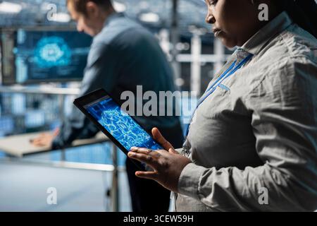 Close up of IT professional in server farm using tablet to improve AI system scalability for increased workloads. Data center engineer using device to adjust artificial intelligence model parameters Stock Photo
