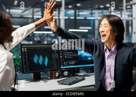 Overjoyed engineers in data center celebrate successfully installing server systems with AI. Delighted server hub workers doing high five, excited after upgrading gear using artificial intelligence Stock Photo
