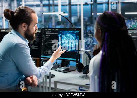 Data center programmers collaborating, working on neural networks AI databases. Server room colleagues talking, using machine learning artificial intelligence on PC to do algorithms improvements Stock Photo