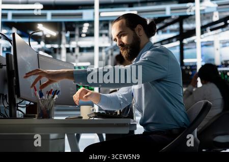 Engineer in data center using PC to update storage arrays software, configuring network virtualization. Man in server room using computer to verify settings, maintaining stable performance Stock Photo