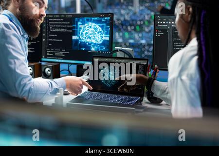 Team leader teaching intern to code in data center, updating AI automation scripts. Server room supervisor guiding trainee during internship, programming artificial intelligence algorithms Stock Photo