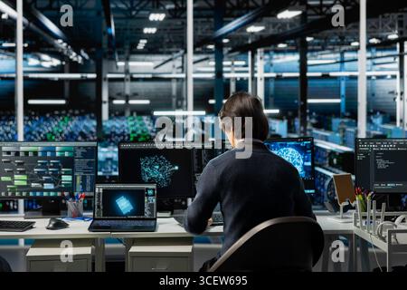 Software developer in data center using PC, managing AI training datasets. IT employee using computer program to oversee machine learning in server room supporting scalable infrastructure for AI apps Stock Photo