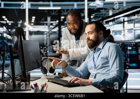 Team of system administrators using computer in server farm, analyzing data. Data center office colleagues doing brainstorming, examining equipment, ensuring system integrity and security Stock Photo