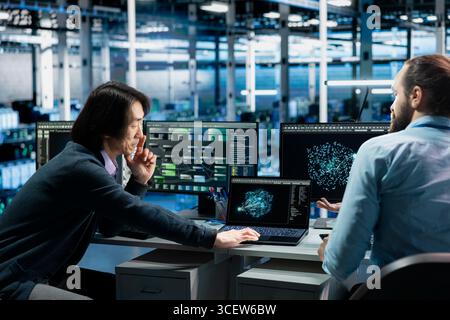 Software developers in data center troubleshooting server connectivity issues using AI. Asian man and technician in server room auditing systems for vulnerabilities using artificial intelligence Stock Photo