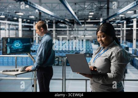 Server farm teamworking admins using laptop to do infrastructure AI machine learning automatization. Data center software developers doing maintenance using artificial intelligence Stock Photo
