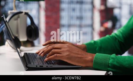 Freelancer creating articles content for his online blog at home desk, writing and working on storytelling with his laptop. Black guy composes social media posts, multitasking. Camera A. Stock Photo