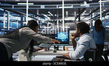 Admin in wheelchair and data center coworker working together using AI node tree software to minimize downtime. Server hub IT expert in disability and colleague using visual programming app, camera A Stock Photo