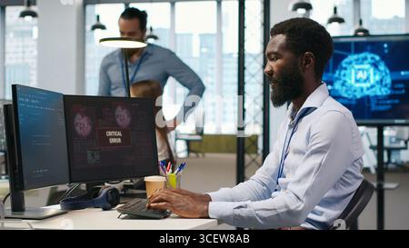 Programmer in office requesting help from coworkers to fix critical error warning. IT employee and colleagues brainstorming how to fix computer bug affecting systems, camera A Stock Photo