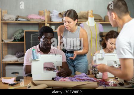 Middle-aged female teacher helping students sew Stock Photo