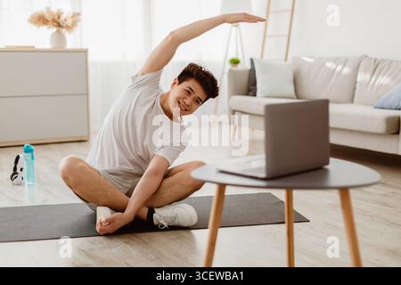 Asian guy doing stretching exercise watching online tutorial Stock Photo