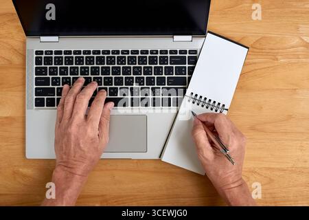 Flat lay of elderly person working from home on a wooden desk. Concept for remote work, online learning, senior lifestyle, and multitasking in Thailan Stock Photo