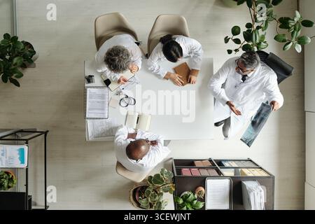 Group of middle aged and senior multiethnic doctors discussing medical records and examining X-ray image around table in hospital meeting room, top view showing collaborative teamwork Stock Photo