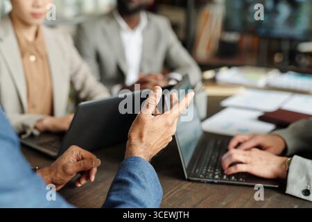 Multiethnic group of middle aged professionals collaborating around laptops during business meeting, hands gesturing while discussing project, focus on teamwork and communication Stock Photo