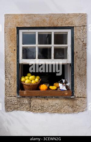 Woven basket with fresh lemons, gourds and a toy windmill on a windowsill, Óbidos, Portugal Stock Photo