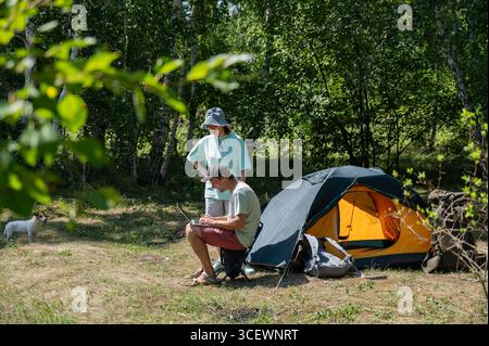 Caucasian man working on laptop in camping. Couple relaxing in nature.  Stock Photo